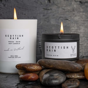 Scottish Rain Candle, Handmade in Scotland, image shows two sizes of candle 100ml and 300ml, the candles are eco-soy, vegan friendly, scent of Scottish Rain,Tin is Black 100ml and the Glass Jar is White 300ml.Tartan Antler is a Scottish Company.