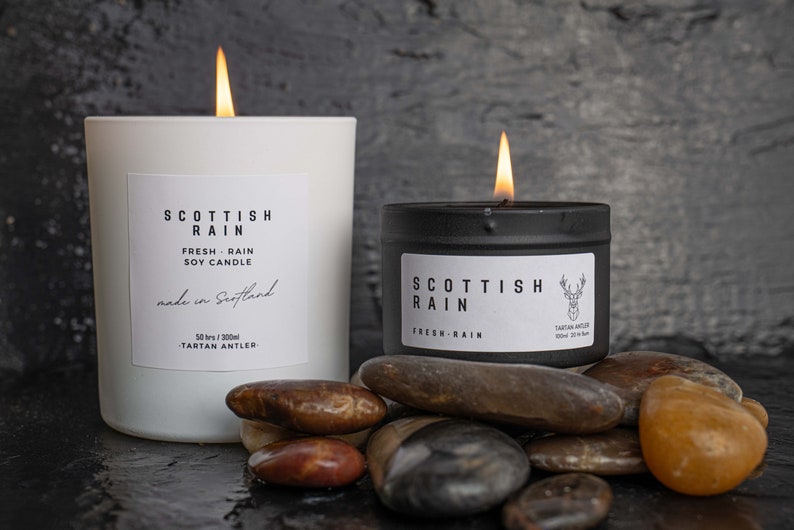 Scottish Rain Candle, Handmade in Scotland, image shows two sizes of candle 100ml and 300ml, the candles are eco-soy, vegan friendly, scent of Scottish Rain,Tin is Black 100ml and the Glass Jar is White 300ml.Tartan Antler is a Scottish Company.