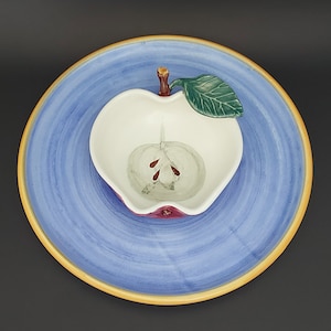May include: A blue and yellow ceramic apple-shaped serving dish with a white interior. The dish has a green leaf and a brown stem.