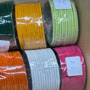 May include: Six rolls of colourful fabric trim, each wrapped in plastic and labelled with a number. The colours are green, yellow, light green, pink, orange, and white.