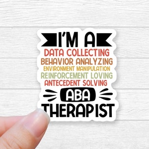 May include: A white sticker with black text that reads "I'm a Data Collecting Behavior Analyzing Environment Manipulation Reinforcement Loving Antecedent Solving ABA Therapist". The text is in a rainbow of colors.
