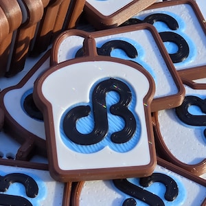 May include: A collection of brown, white, and blue bread-shaped objects. Each piece has a white center with a black symbol and a blue background. The objects are stacked and scattered, creating a playful and eye-catching display.