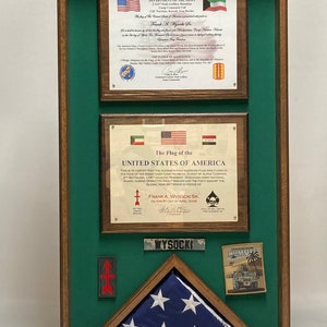 May include: A wooden shadow box display case with a green velvet backing containing two framed military certificates, a name plate reading WYSOCKI, a rectangular red arrow patch, a square Humvee patch, and a folded American flag in a triangle.