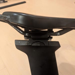 Może przedstawiać: Czarne siodełko rowerowe zamontowane na sztycy z mechanizmem zaciskowym. Na prętach siodełka widnieje nadruk Use 7X9 mm Clamp oraz Max. Zestaw zawiera czarną sztycę oraz wspornik montażowy z widocznymi metalowymi śrubami mocującymi.