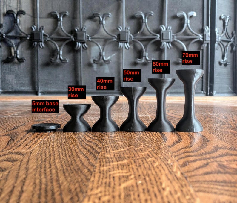 Pu&ograve; includere: Un set di sei supporti neri a forma di clessidra di varie altezze. Le etichette indicano una base di 5mm, seguite da opzioni di 30mm, 40mm, 50mm, 60mm e 70mm. Ogni pezzo presenta una sezione centrale concava e una superficie superiore piatta.