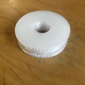 以下が含まれることがあります： 中央に穴が開いた白いプラスチックのスプール。スプールは3Dプリントされたプラスチックでできています。