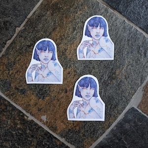 May include: Three blue and white stickers featuring a stylized illustration of a person with blue hair and eyes. The person is depicted with their arms crossed over their chest and a floral pattern on their skin.