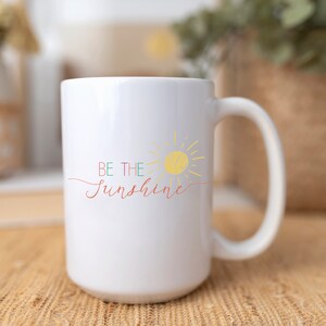 May include: White ceramic mug with a yellow sun and the text "BE THE SUNSHINE" in colorful script.