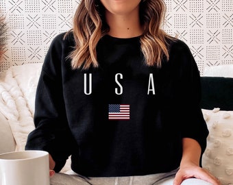 May include: Black sweatshirt with the word "USA" in white capital letters and a small American flag graphic. The sweatshirt is a crew neck style and is made of a soft material.