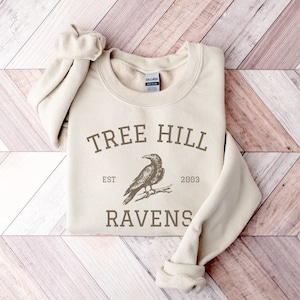 May include: A beige sweatshirt with a brown graphic print of a raven and the text "Tree Hill Est 2003 Ravens".
