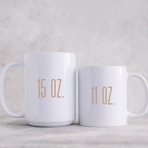 May include: Two white ceramic mugs with black text. The larger mug says "15 oz." and the smaller mug says "11 oz."