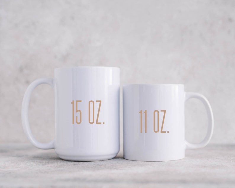May include: Two white ceramic mugs with black text. The larger mug says "15 oz." and the smaller mug says "11 oz."