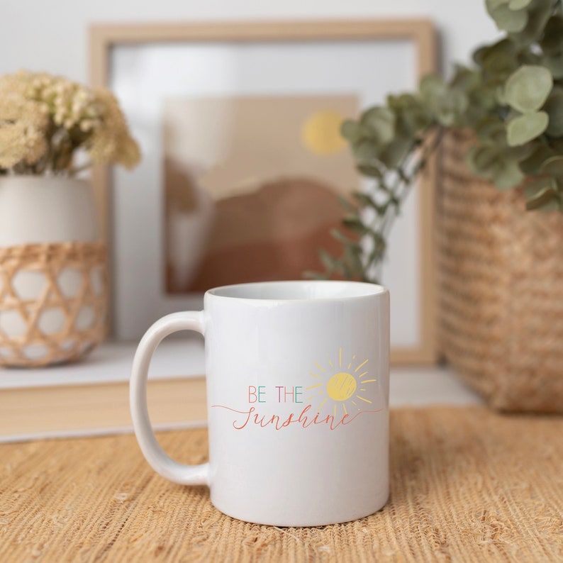 May include: White ceramic mug with a yellow sun and the text "BE THE SUNSHINE" in colorful script.