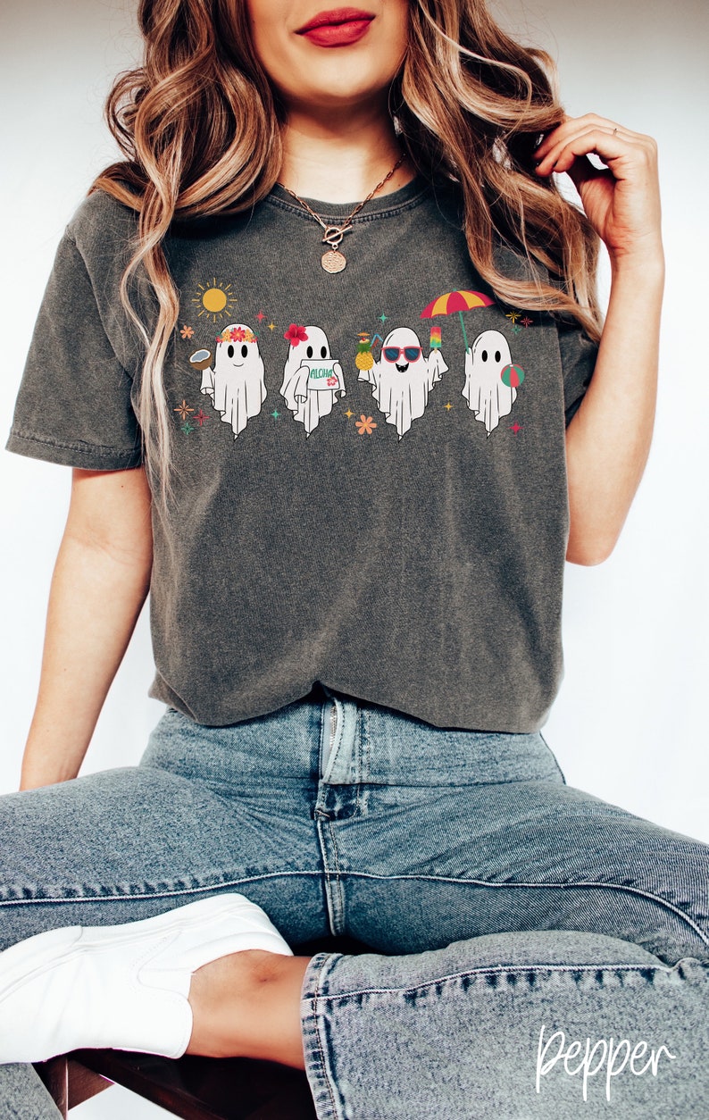 K&ouml;nnte beinhalten: Ein dunkelgraues T-Shirt mit einem Aufdruck von f&uuml;nf Geistern, die Sonnenbrillen tragen, Getr&auml;nke halten und den Strand genie&szlig;en. Die Geister tragen Blumenkr&auml;nze und halten Strandaccessoires wie einen Strandball, eine Ananas und einen Cocktail.
