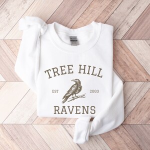 May include: White sweatshirt with a brown graphic print of a raven and the text "Tree Hill Est 2003 Ravens".