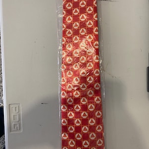 May include: A red tie with a white and yellow geometric pattern. The pattern features a repeating design of a triangle inside a circle.