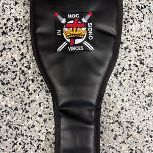 May include: Black leather sheath with a stitched border. The sheath features an embroidered emblem with a crown, swords, and the text "HOC SIGNO VINCES" in white and red.
