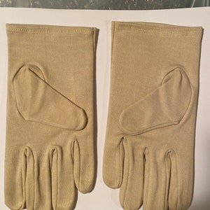 May include: A pair of beige gloves with a smooth texture. The gloves have a seam down the middle of each finger and a small patch on the palm.