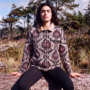 May include: A long-sleeve button-up jacket featuring a dark purple and cream damask floral pattern, a tan sherpa collar, and a single chest pocket. The jacket is paired with solid black leggings, creating a cohesive look with a structured collar.