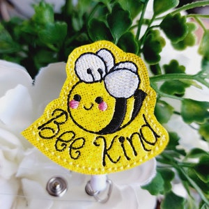 May include: Yellow embroidered bee with black stripes and white wings on a yellow background with the text "Bee Kind" in black embroidery.