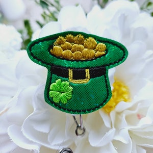 May include: A green leprechaun hat with a gold coin design and a shamrock, attached to a retractable badge holder.