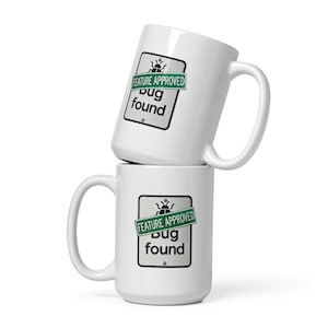 May include: Two white ceramic mugs with a green and black graphic of a bug with the text "FEATURE APPROVED Bug found".