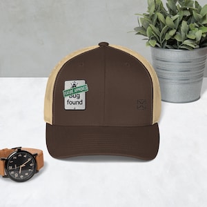 May include: A brown and tan trucker hat with a green and white patch that says "Feature Approved Bug Found".