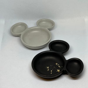 May include: Two ceramic Mickey Mouse shaped dishes. One dish is gray and the other is black. The black dish has gold flakes inside.