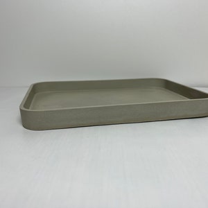 May include: A light gray rectangular tray with a slightly raised edge. The tray is made of a textured material and has a smooth, matte finish.