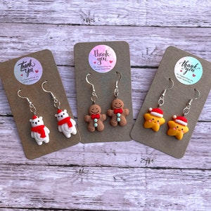 May include: Three pairs of Christmas-themed earrings displayed on brown card stock. The earrings are silver with a white polar bear, a gingerbread man, and a yellow star with a red Santa hat. Each card has a round sticker with the text "Thank you for supporting my small business".