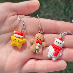 May include: Three pairs of Christmas-themed earrings featuring a gingerbread man, a star with a Santa hat, and a polar bear wearing a red scarf.