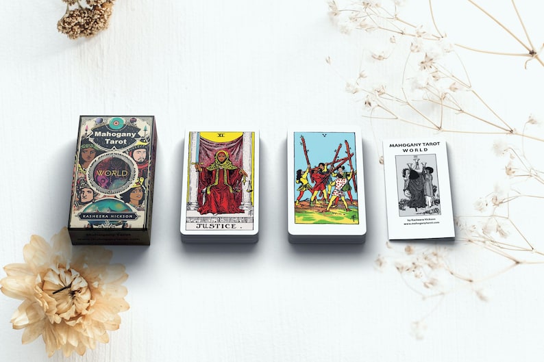 May include: An overhead shot of a tarot card set with a box and three card stacks. The box reads "Mahogany Tarot World" with illustrations. The cards show various tarot imagery, including "Justice" and "World". The set is on a white surface.