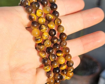 May include: A stack of four bracelets made with tiger's eye beads. The beads are round and have a mix of brown, gold, and black colors.