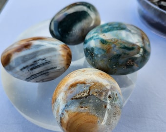 Puede incluir: Cuatro piedras de ágata pulidas con patrones marrones, blancos y verdes. Las piedras están dispuestas sobre una base circular blanca.