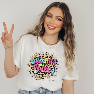 Pu&ograve; includere: T-shirt bianco con grafica colorata "Summer Vibes". Il design presenta uno sfondo con stampa leopardata con le parole in una sfumatura arcobaleno. La maglietta &egrave; uno stile estivo casual.