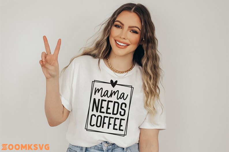 Pode incluir: Camiseta branca com texto preto que diz "mama needs coffee" dentro de um quadro quadrado preto com um pequeno cora&ccedil;&atilde;o preto acima do texto.