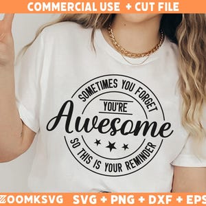 Op de afbeelding: Wit T-shirt met een zwarte cirkelvormige afbeelding met de tekst "Soms vergeet je dat je geweldig bent, dus dit is een herinnering".