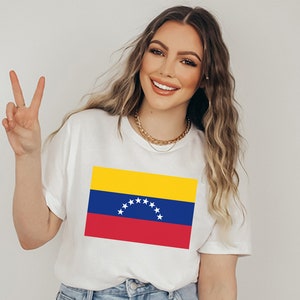 May include: A white t-shirt with a printed image of the Venezuelan flag. The flag is yellow, blue, and red with a star-shaped arc in the center.