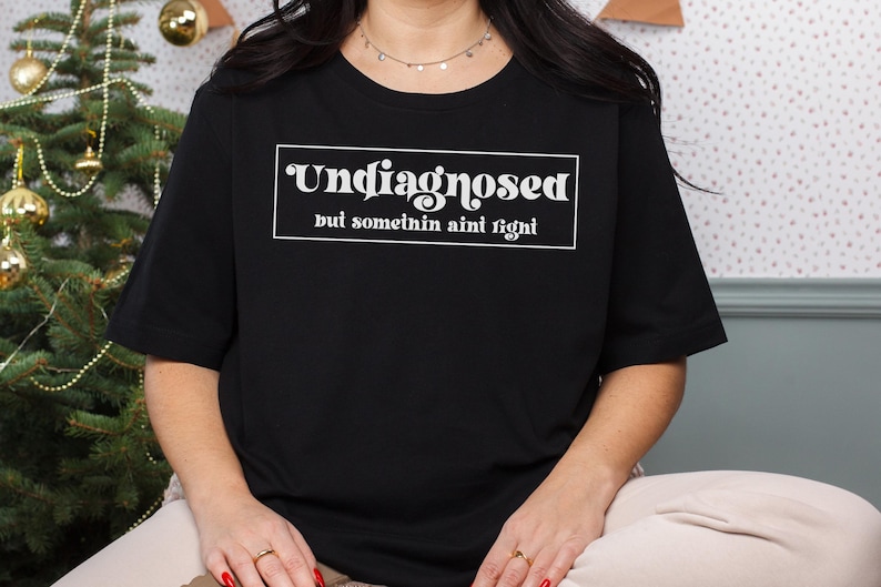May include: Black t-shirt with white text that reads "Undiagnosed but somethin ain't right".