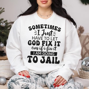 May include: White sweatshirt with a black graphic print that reads "Sometimes I Just Have To Let God Fix It Cus If I Fix It I Am Going To Jail".