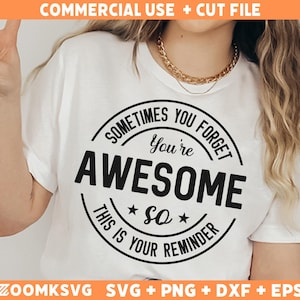 Op de afbeelding: Wit T-shirt met een zwart cirkelvormig ontwerp met de tekst "Soms vergeet je dat je geweldig bent. Dit is je herinnering."