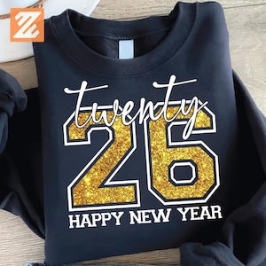 Puede incluir: Sudadera negra con el texto "twenty 26 HAPPY NEW YEAR" en blanco y purpurina dorada. La sudadera de cuello redondo es ideal para celebrar el Año Nuevo.