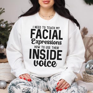 May include: White sweatshirt with black text that reads "I need to teach my facial expressions how to use their inside voice."