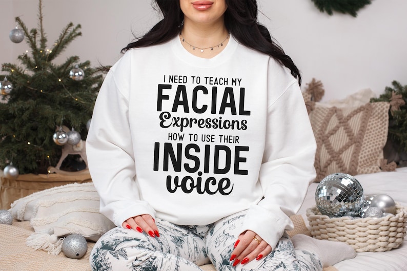 May include: White sweatshirt with black text that reads "I need to teach my facial expressions how to use their inside voice."