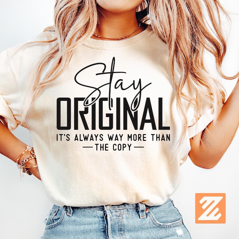 Puede incluir: Camiseta color crema con las palabras "Stay Original" en escritura negra y en negrita. El texto "It's always way more than - the copy -" est&aacute; debajo. La camiseta la lleva una persona con pelo largo y rubio ondulado.