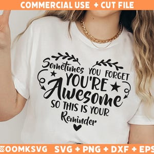 Op de afbeelding: Wit T-shirt met een zwart hartontwerp met de tekst "Soms vergeet je dat je geweldig bent, dus dit is een herinnering".