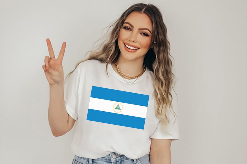 May include: A white t-shirt with a blue and white Nicaraguan flag printed on the front. The flag features a triangle with a green tree and a gold border.