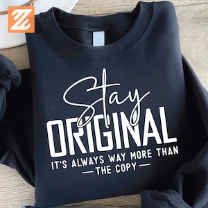 May include: Black sweatshirt with the words "Stay Original" in white script and block letters. Below the main text is the phrase "It's Always Way More Than The Copy" in white, sans-serif font.