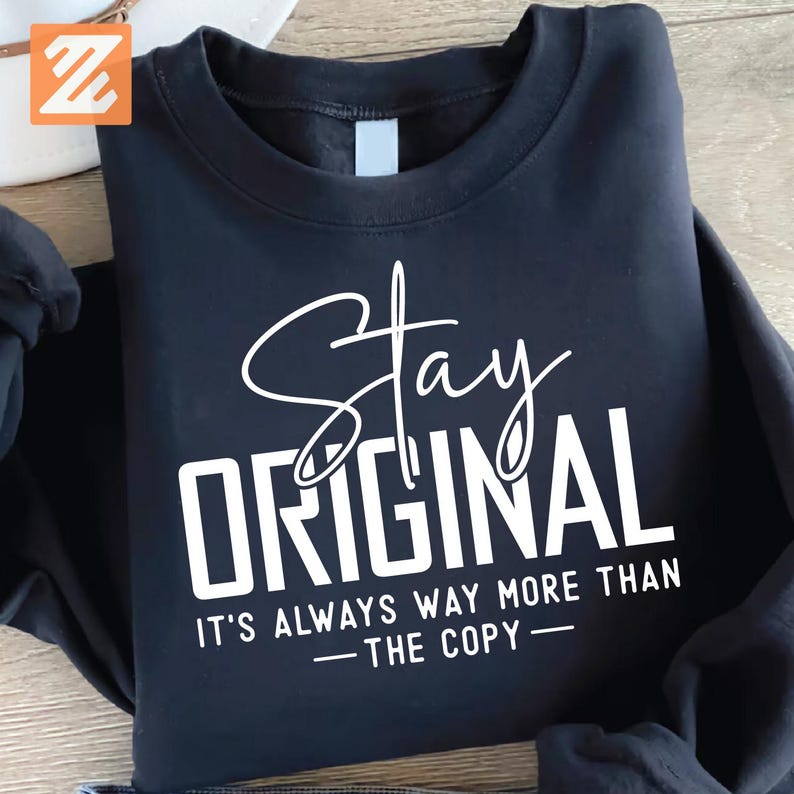 Puede incluir: Sudadera negra con las palabras "Stay Original" en escritura blanca y letras de bloque. Debajo, la frase "It's Always Way More Than The Copy" est&aacute; impresa en blanco.