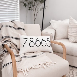 May include: A white armchair with a black and white striped throw blanket and a white pillow with the number "78665" printed in black.